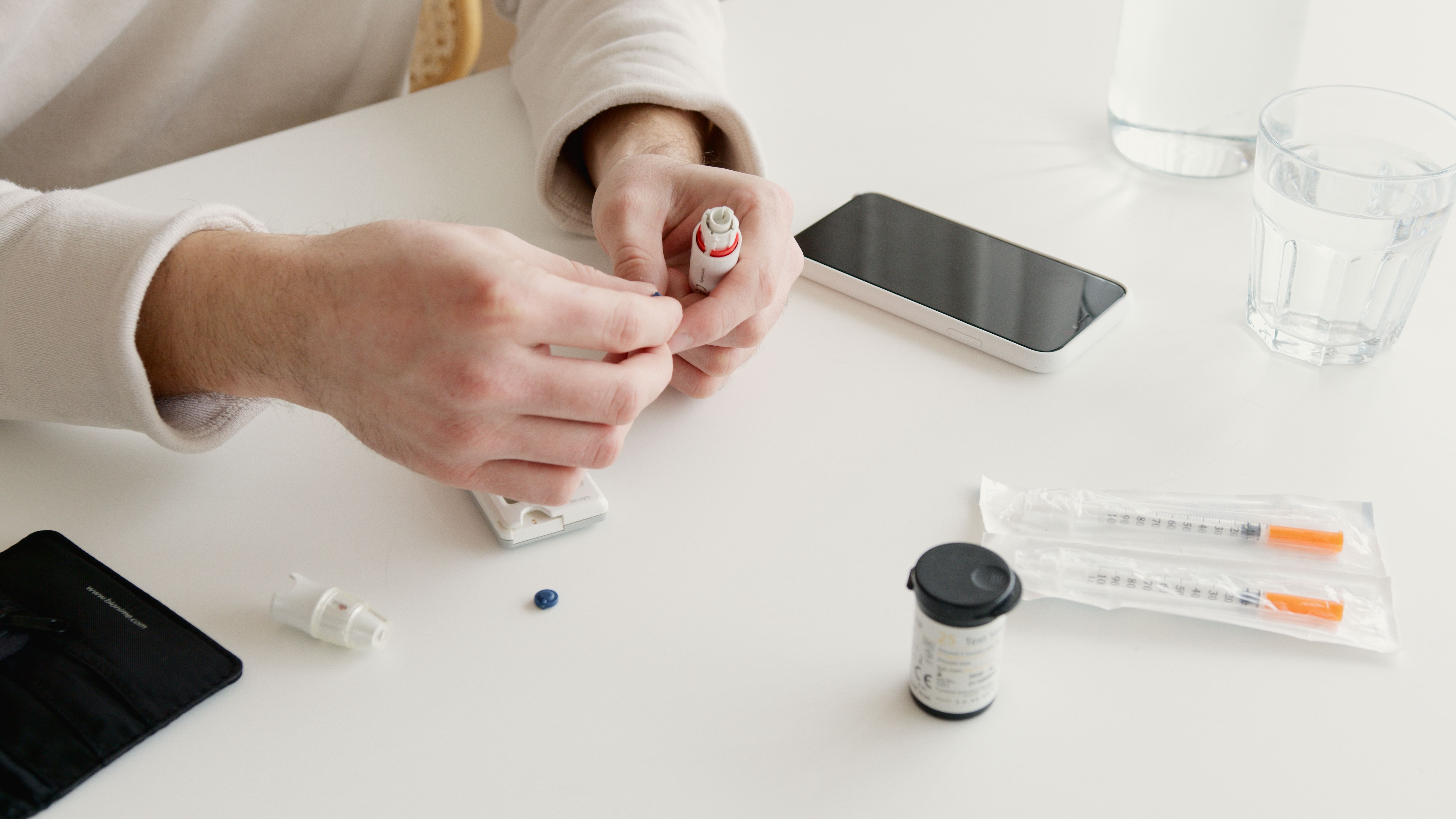 Hands preparing a blood glucose meter beside a phone and glass of water